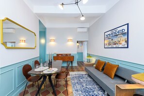 A modern dining area with a round table, chairs, and a sofa. There is a large mirror, wall-mounted lights, and a poster on the wall. - Stylish Apartment in the Heart of Trastevere (Roma)