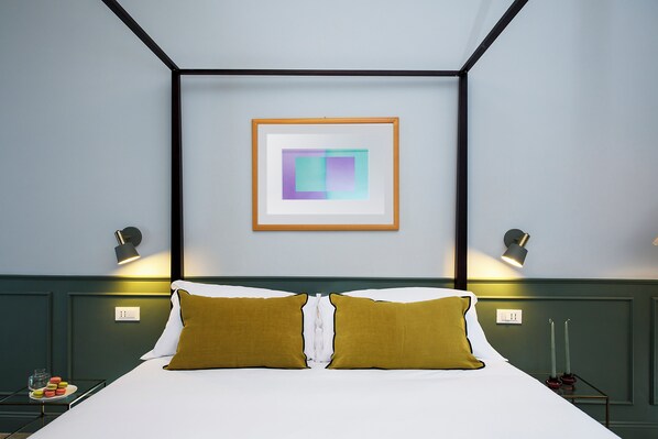 A neatly arranged hotel room with a bed, two bedside lamps, a framed abstract artwork, and a small table with a plate of macarons. - Stylish Apartment in the Heart of Trastevere (Roma)