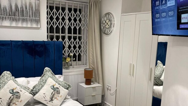 Ein modernes Schlafzimmer mit einem Bett, einem Fernseher, einem Kleiderschrank und einem Fenster mit Vorhängen.