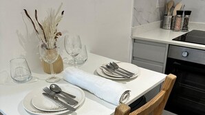 Ein Esstisch mit Geschirr, Besteck und Gläsern, eine Vase mit Trockenpflanzen und ein Holzstuhl.