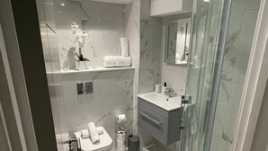 Ein modernes Badezimmer mit Duschkabine aus Glas, Marmorboden, Waschbecken mit Spiegel darüber und Toilette mit Handtuch darauf.