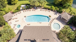 Vista aérea de un complejo turístico con una piscina grande, sillas de descanso y un jacuzzi.