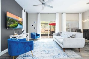 A modern living room with a flat-screen TV, a white sofa, blue armchairs, a coffee table, and a ceiling fan. - Near Disney Premium Location Coral Cay Resort (Kissimmee)