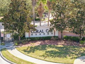 A sign for Coral Cay Resort with a gated entrance, a well-maintained lawn, and surrounding trees. - Near Disney Premium Location Coral Cay Resort (Kissimmee)