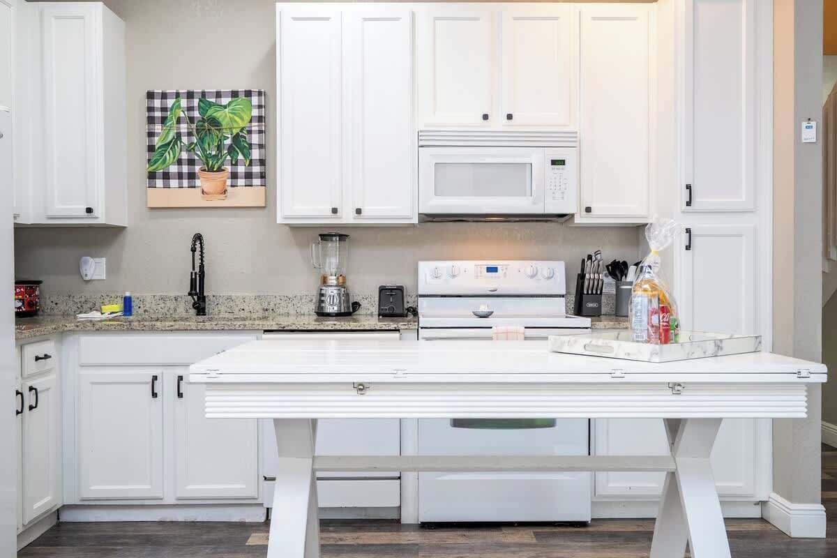 A kitchen with white cabinets, a microwave, a stove, a blender, and a countertop with various items.
