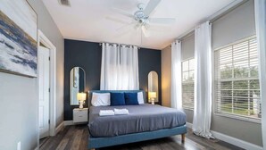 Un dormitorio con cama, ventilador de techo, mesita de noche, espejo y ventana con persianas.