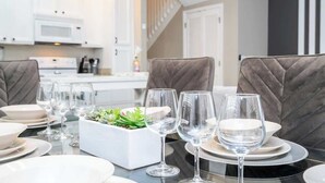 Un comedor con una mesa preparada para cuatro personas, armarios blancos, un microondas y una escalera al fondo.