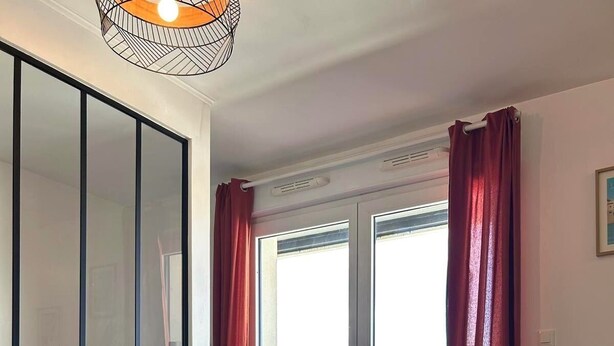 Una habitación de hotel moderna con televisión, una mesa de comedor con planta, un sofá y un balcón con puerta de vidrio corredera.