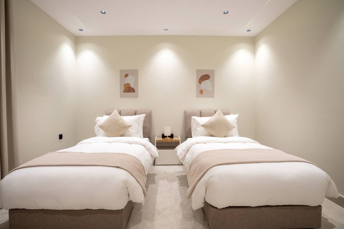 Quarto de hotel com duas camas, uma mesa de cabeceira e obras de arte nas paredes.