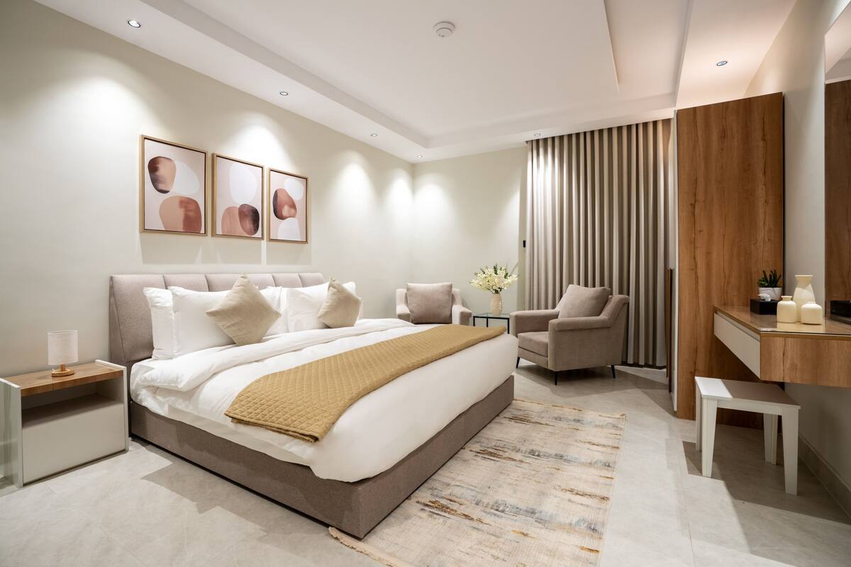 Quarto moderno com cama grande, mesas de cabeceira, escrivaninha e uma cadeira.