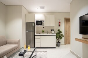 A modern kitchen with white cabinets, a microwave, a refrigerator, and a potted plant.