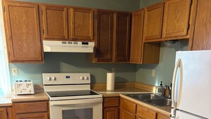 A kitchen with wooden cabinets, a white stove, a sink, and a refrigerator. - Charming 2-bedroom Getaway in Broadus (Broadus)