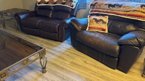 A living room with two leather sofas, a glass coffee table, and a wall-mounted air conditioner. - Charming 2-bedroom Getaway in Broadus (Broadus)