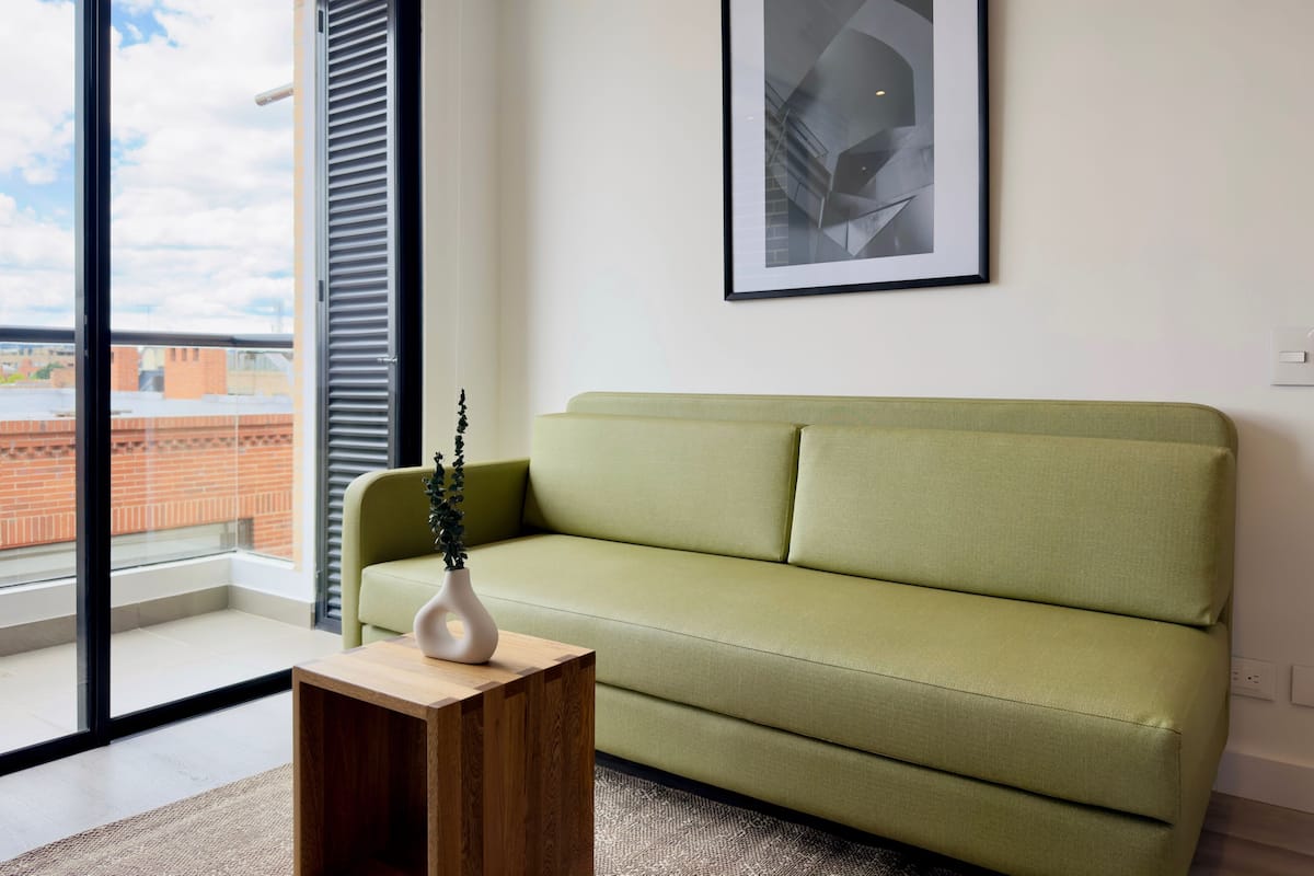 A modern living room with a green sofa, a wooden coffee table, and a framed abstract artwork on the wall.