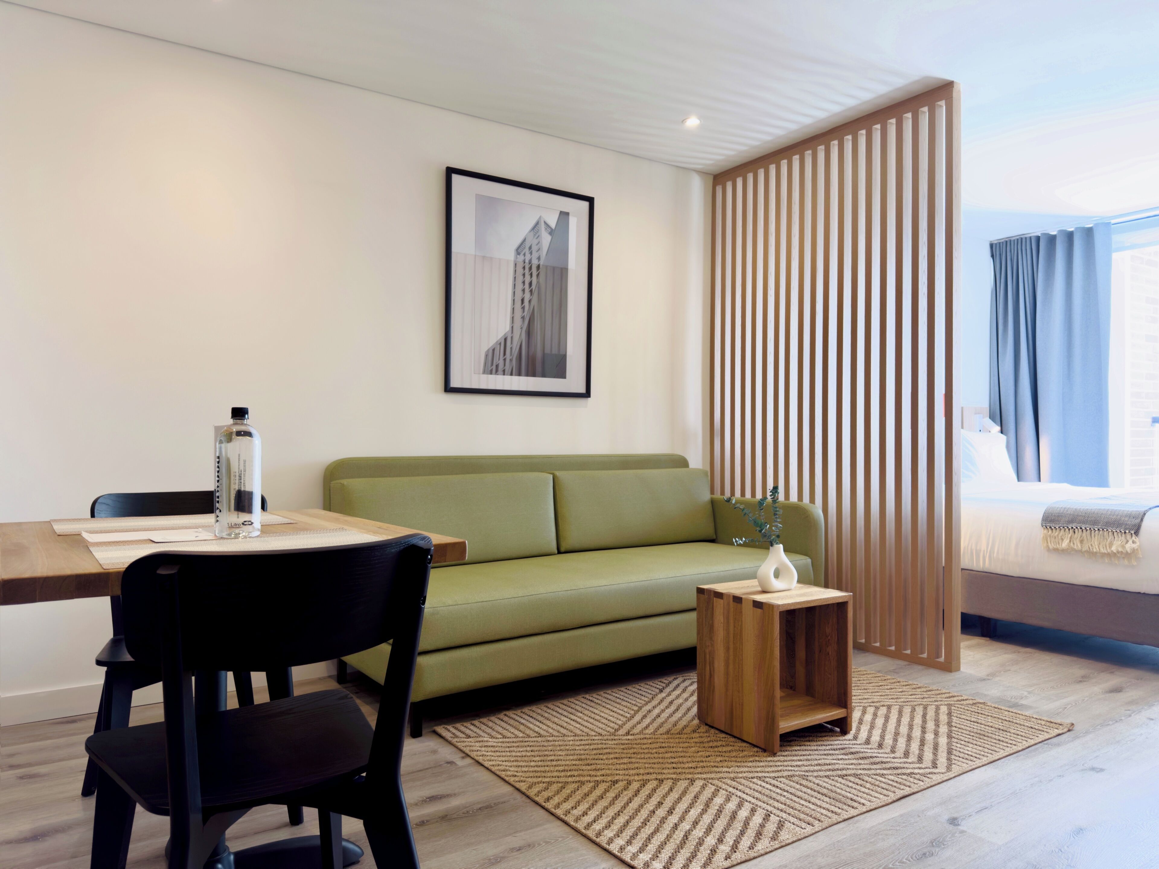 A modern living room with a green sofa, a wooden coffee table, a framed picture on the wall, and a window with curtains.