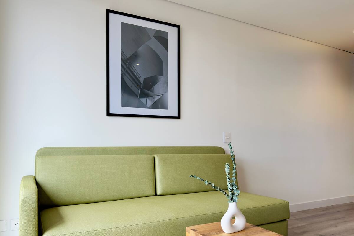 A green sofa against a white wall with a framed abstract artwork above it.