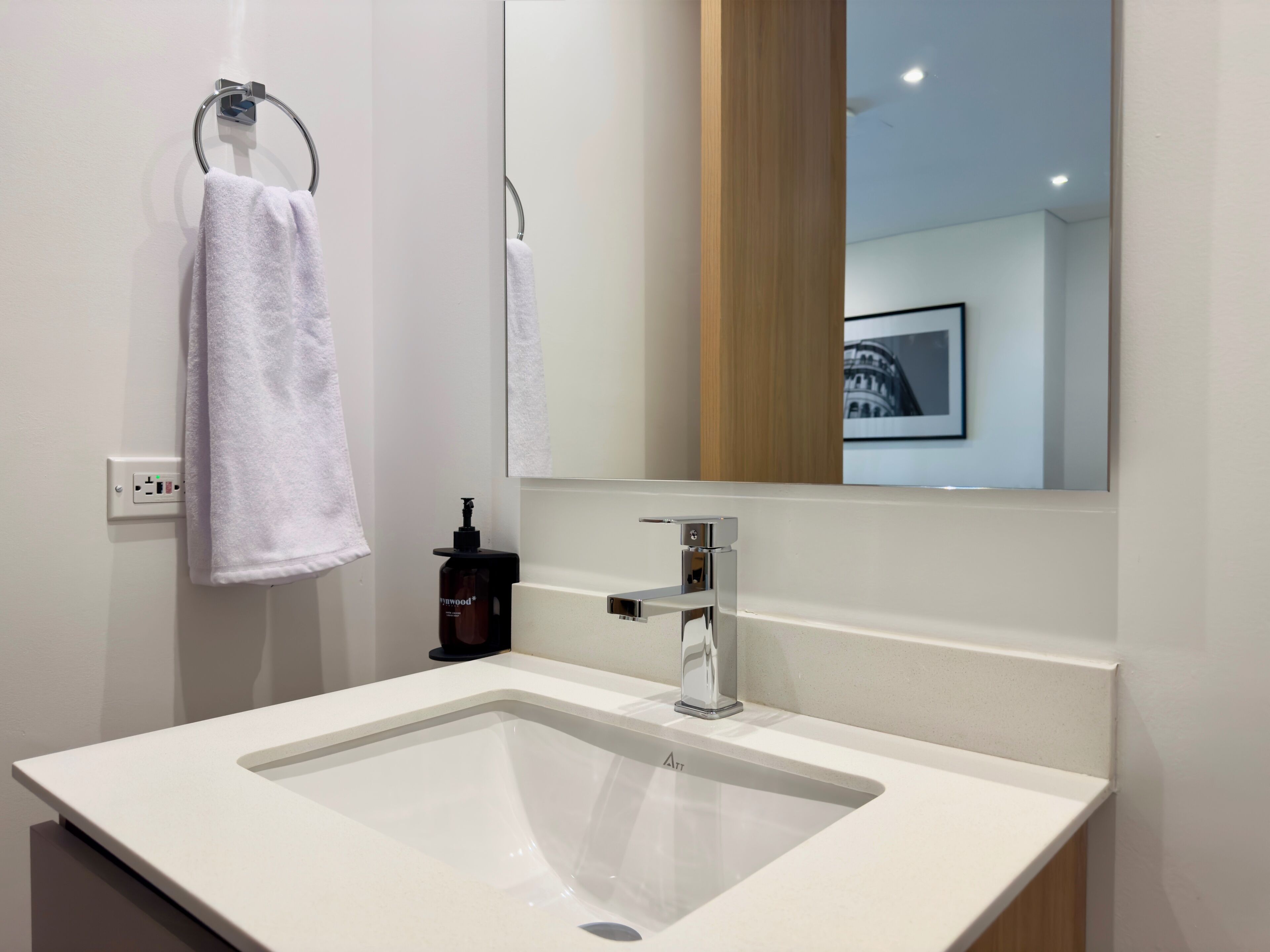 A modern bathroom with a white sink, a mirror, and a towel rack.