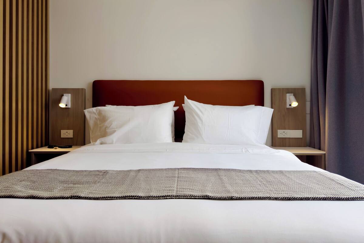 A neatly made bed with white linens, a brown headboard, and two bedside lamps.
