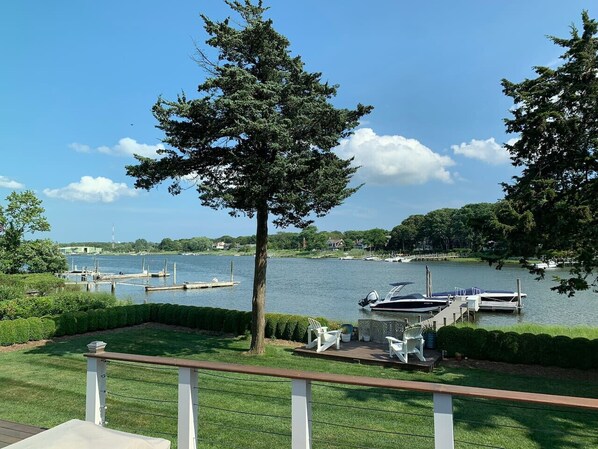 A lakeside view with docked boats, a grassy area with chairs, and a large tree.