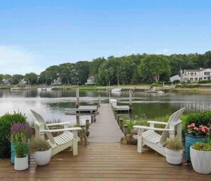 A wooden dock leading to a calm lake with boats, surrounded by greenery and houses. - Waterfront tranquility near Sag Harbor Village (Sag Harbor)
