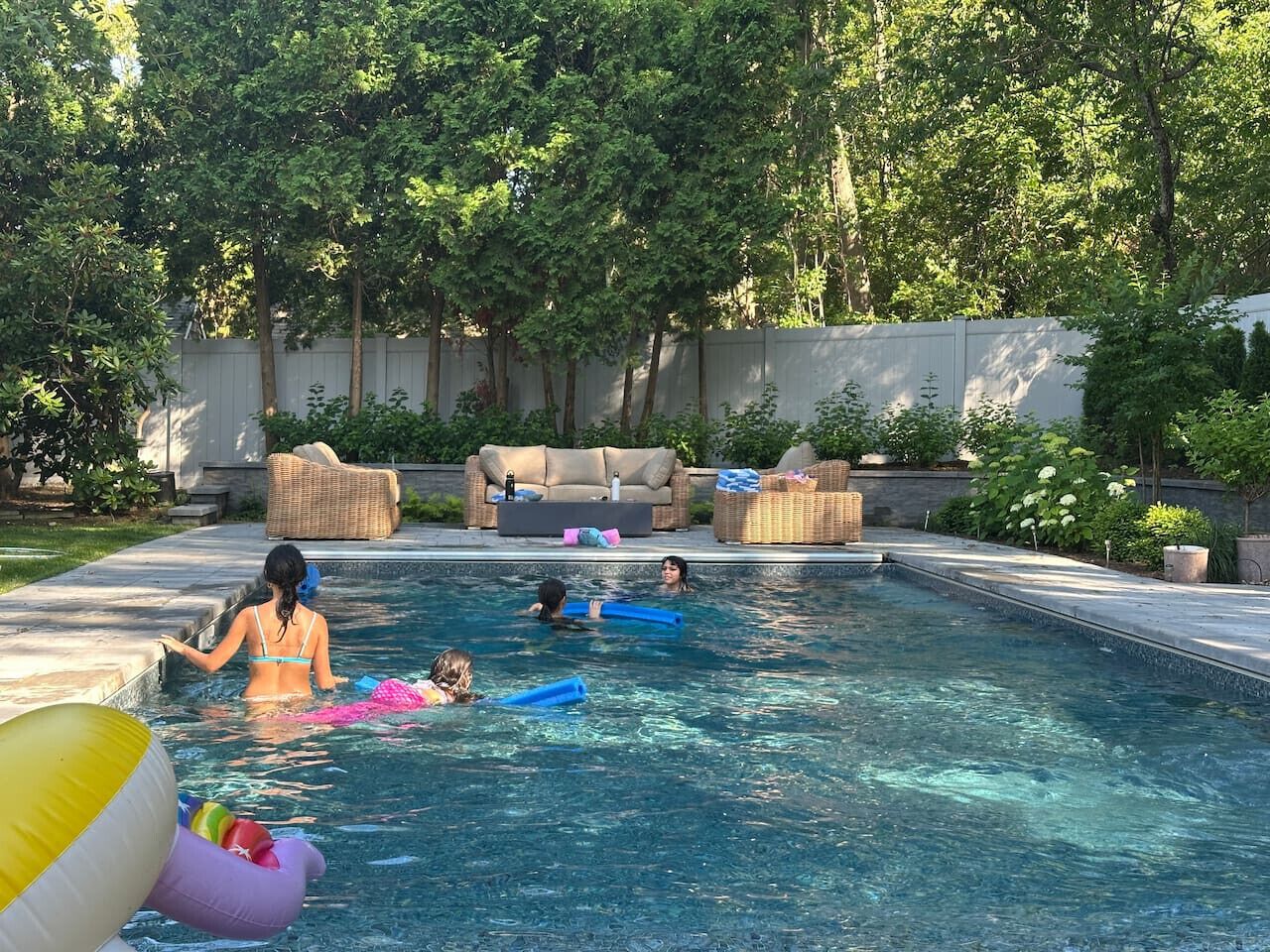 A swimming pool with people, lounge chairs, and a garden in the background.