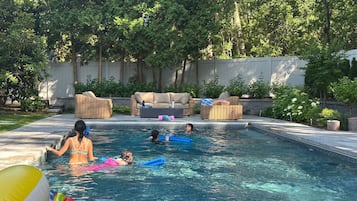 A swimming pool with people, lounge chairs, and a garden in the background.