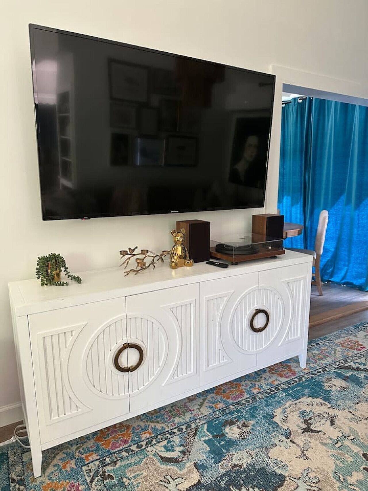 Un mueble multimedia blanco con un televisor de pantalla plana, adornos y una alfombra estampada.