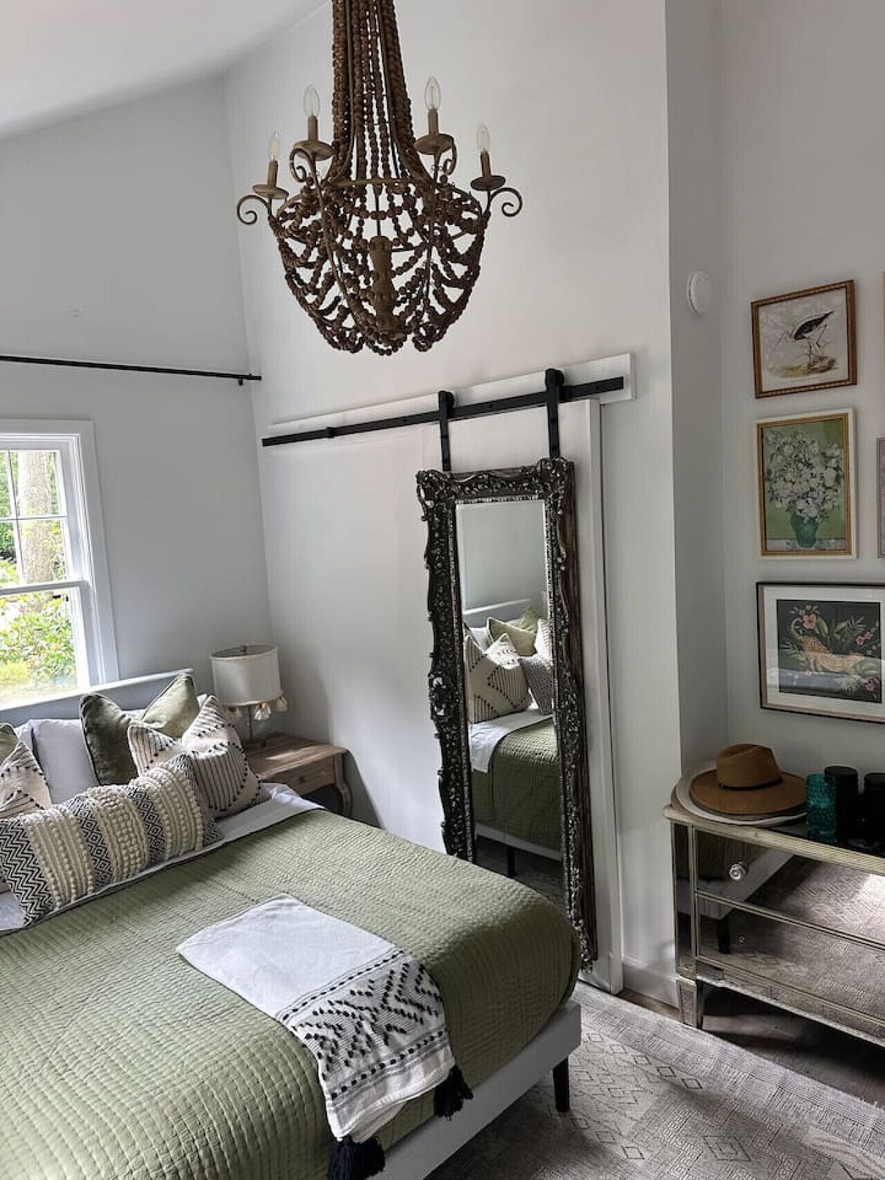 Une chambre à coucher avec un lit, un grand miroir, un luminaire suspendu et des œuvres d’art accrochées au mur.