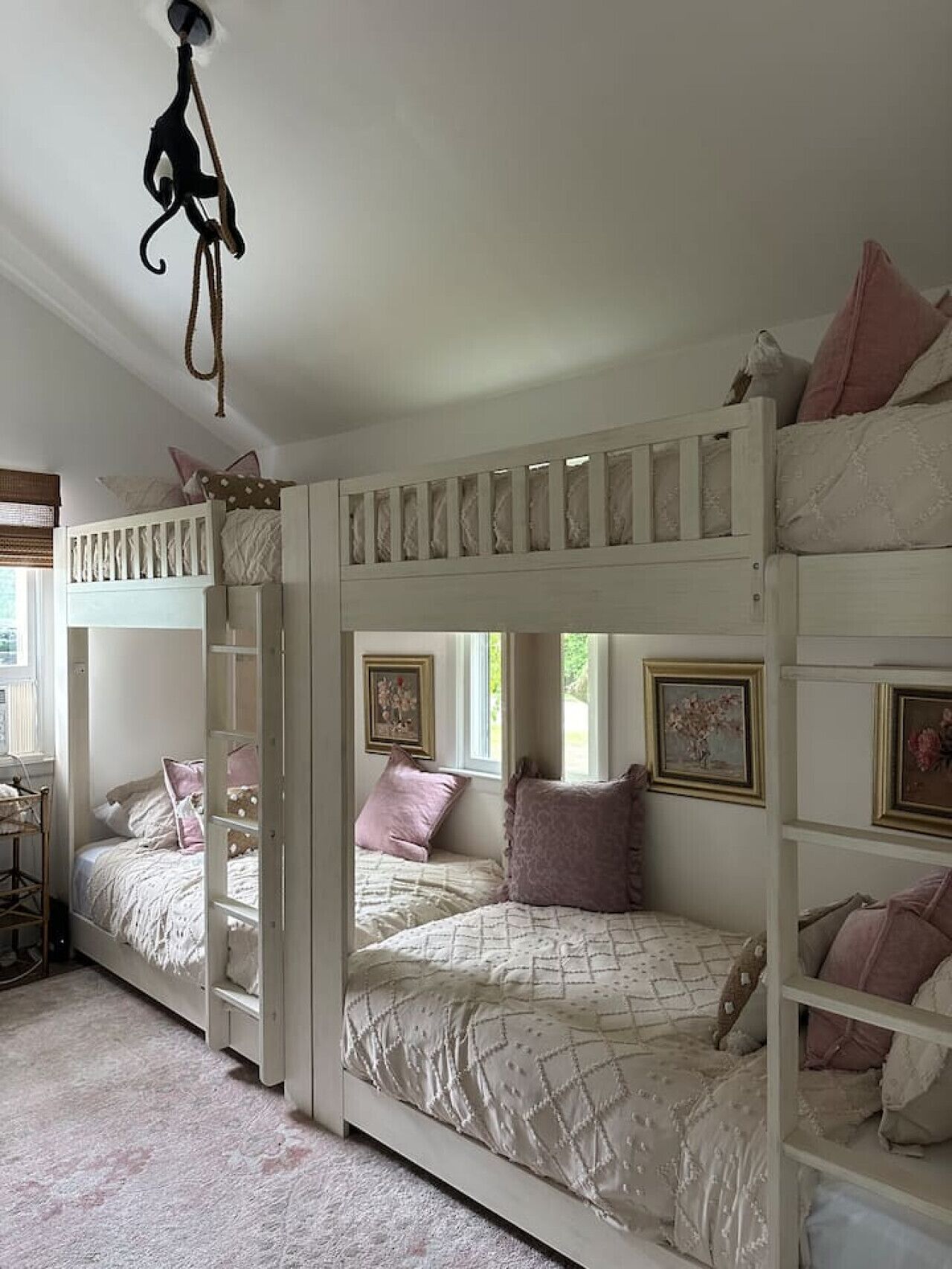 Une chambre avec un lit superposé, une échelle, deux lits et un luminaire suspendu.