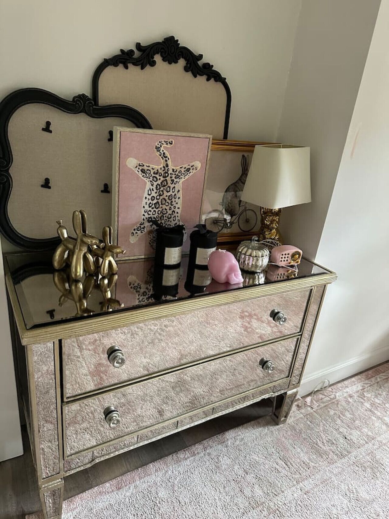 Um aparador estilo vintage com espelho, uma obra de arte com estampa de leopardo e vários objetos decorativos.