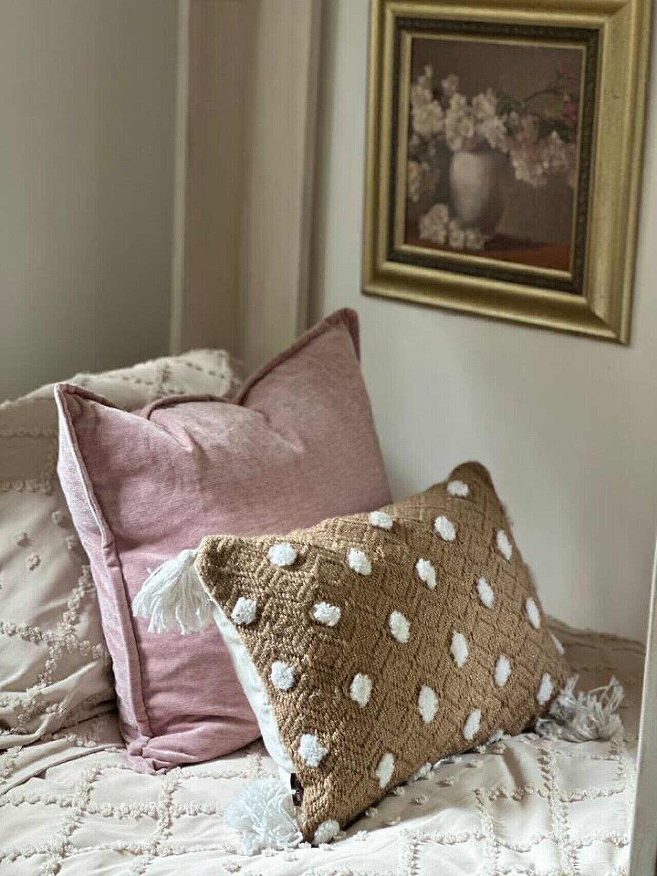 Ein Bett mit einer gemusterten Decke, einem rosa Kissen und einem braunen Strickkissen.