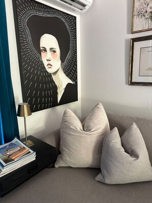 A modern living room with a sofa, pillows, a magazine, and a framed picture on the wall.