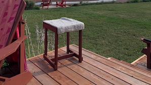 Une terrasse avec un plancher en bois, une petite table recouverte d’une nappe blanche et deux chaises Adirondack rouges.