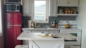 Une cuisine avec des meubles blancs, un réfrigérateur rouge, une cuisinière blanche et un plan de travail en marbre.