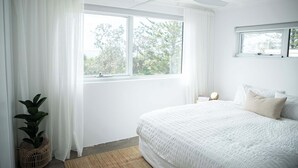 A bedroom with a large bed, a ceiling fan, a window with curtains, and a potted plant.
