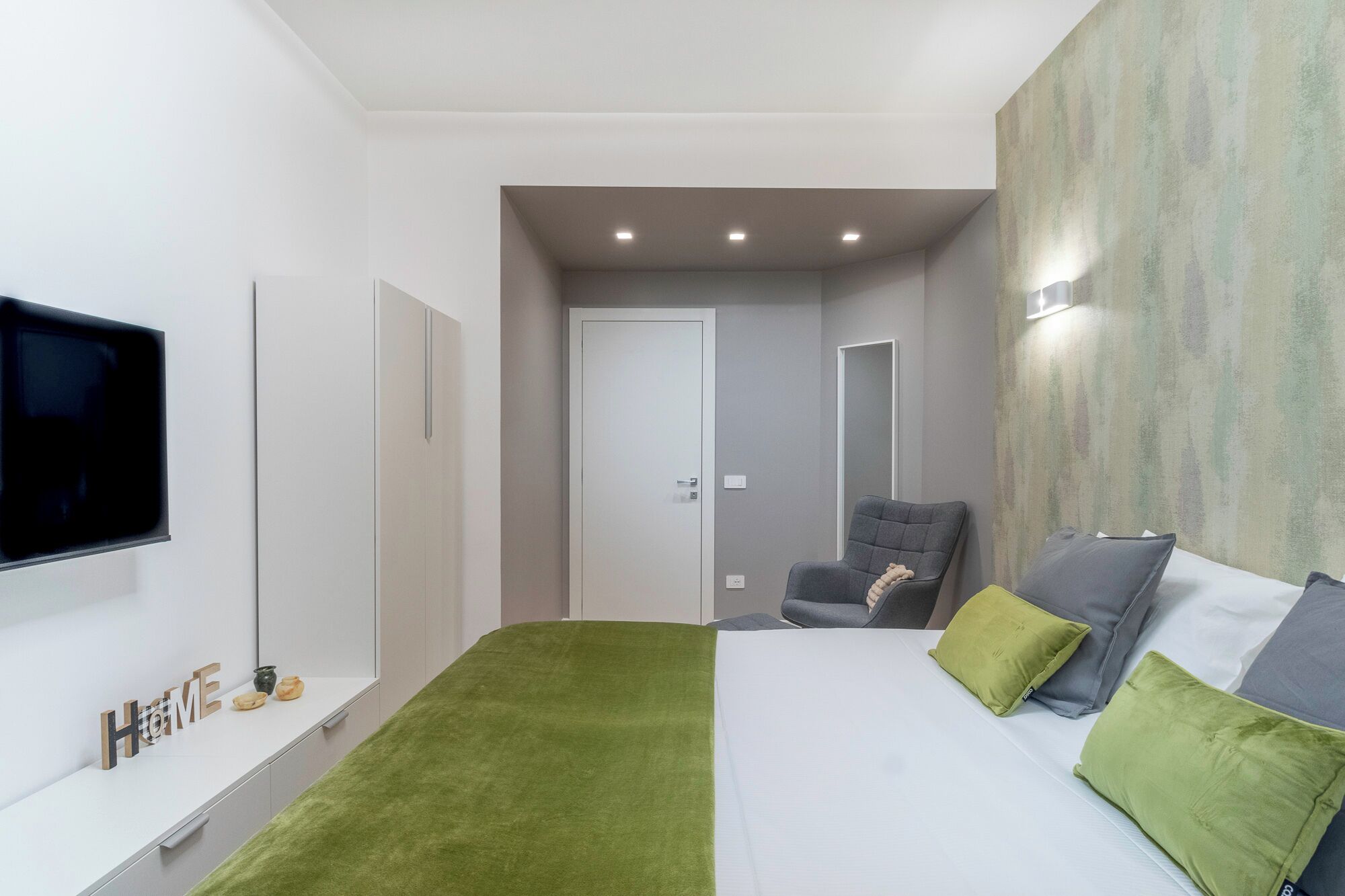A modern bedroom with a bed, a chair, a TV, and a wardrobe.