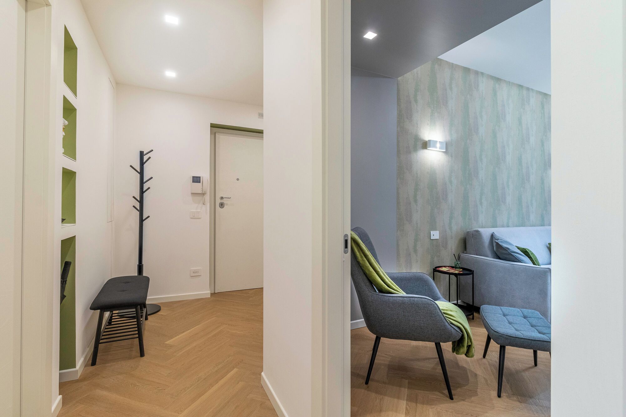 A modern interior with a wooden floor, a grey sofa, and a chair with a green throw.