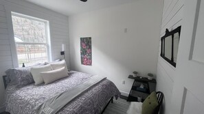 Een slaapkamer met een bed, nachtkastje, raam en een aan de muur hangend schilderij.