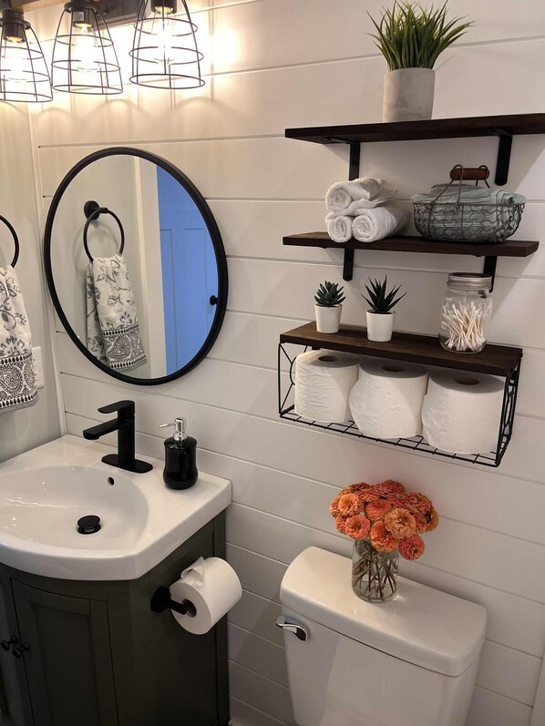 Een badkamer met een ronde spiegel, een wastafel, toilet en planken met handdoeken en planten.