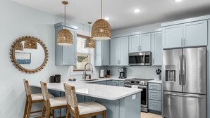 Eine moderne Küche mit hellblauen Schränken, einem Edelstahl-Kühlschrank, einer Mikrowelle und einer großen Kochinsel mit Barhocker.