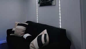 A modern room with a black sofa, a wall-mounted picture, and LED strip lighting along the ceiling edges. - Welcoming studio in Roseville perfect for a cozy getaway (Roseville)