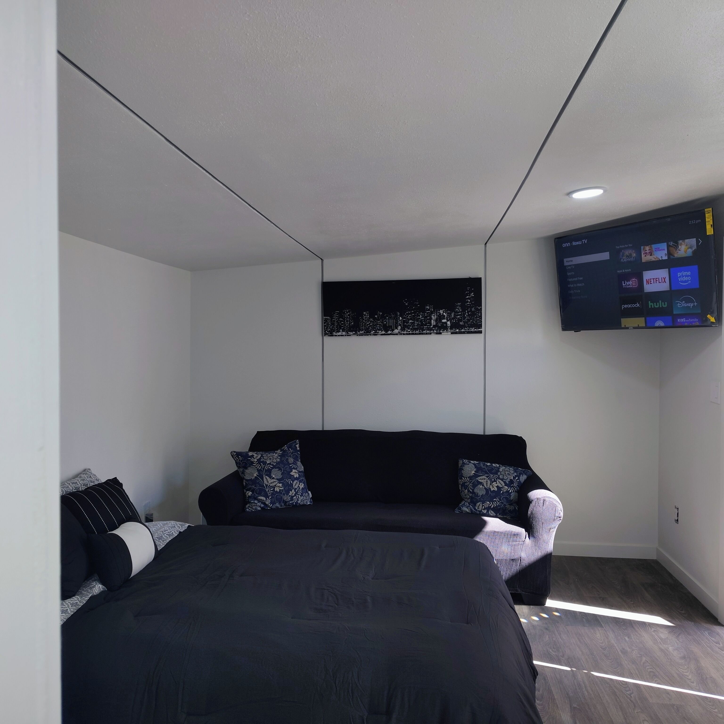 A modern bedroom with a bed, a sofa, and a mounted TV displaying various streaming services.