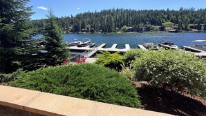 Vista sobre un lago con barcos amarrados, una terraza de madera y un bosque denso al fondo.