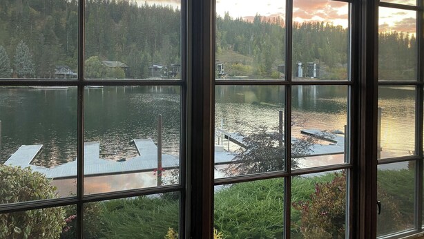Vista a través de una ventana de un lago con barcos, un muelle y una zona boscosa.