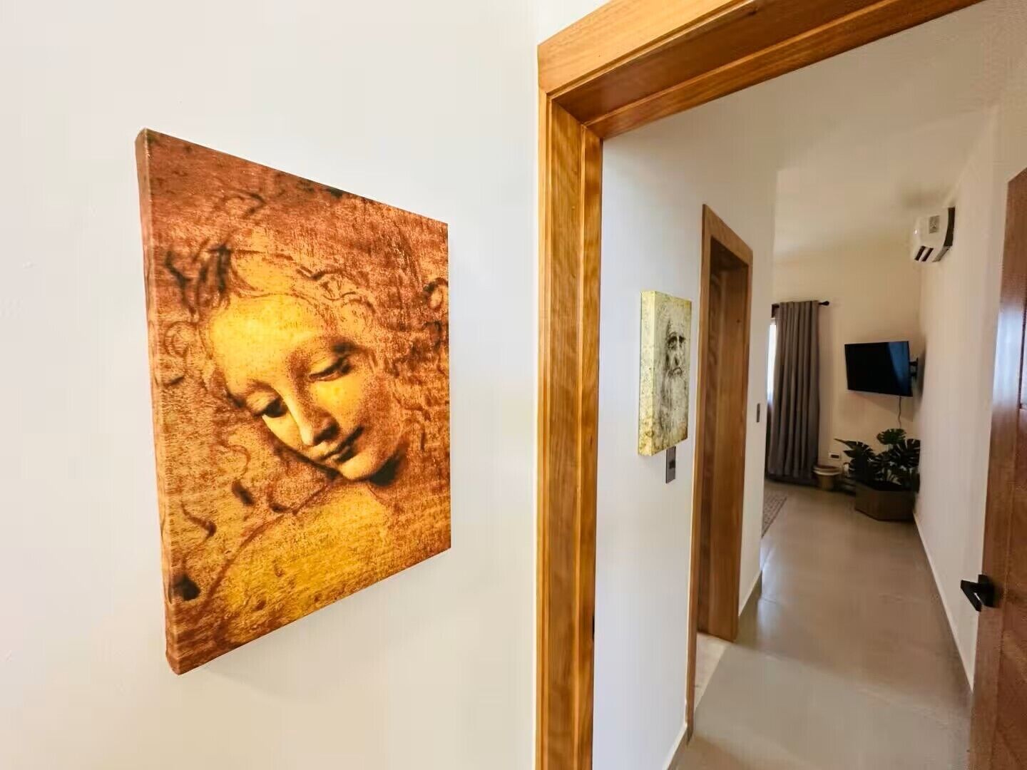 A hallway with a wooden door frame, a painting on the wall, and a television mounted on the wall.