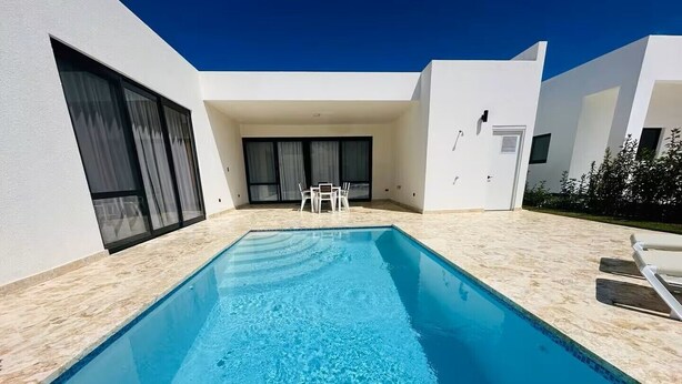 A rectangular swimming pool with clear blue water, surrounded by a light-colored tiled deck.