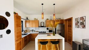 A modern kitchen with wooden cabinets, a central island with stools, a refrigerator, and pendant lighting.