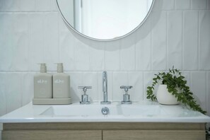 A bathroom with a white sink, two bottles of lotion, a mirror, and a potted plant. - El Parche Bilinga | Stylish 2BR by the Beach, Unit 4 (Bilinga)