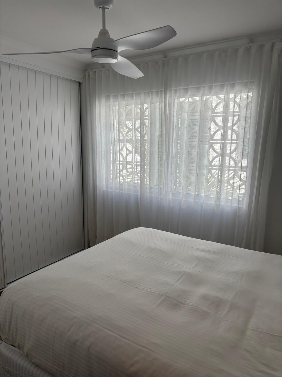 A bedroom with a bed, a ceiling fan, and sheer curtains.