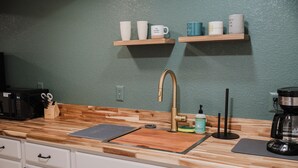 A kitchen with a wooden countertop, a stainless steel sink, a coffee maker, and a shelf with cups. - NEW Spacious Park-view Walk-out Basement near Coffee and Trails (Colorado Springs)
